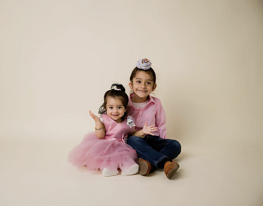Using portrait of a big brother sitting on the floor with his one year old sister wearing matching colored clothes and smiling for her birthday images taken for her butterfly first birthday party in Eastampton, New Jersey.
