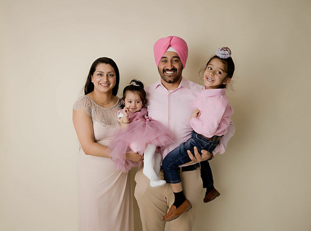 Family portrait of a woman and man smiling with their two children wearing matching colored clothes and posing for their daughters birthday cake pic in Medford, New Jersey.