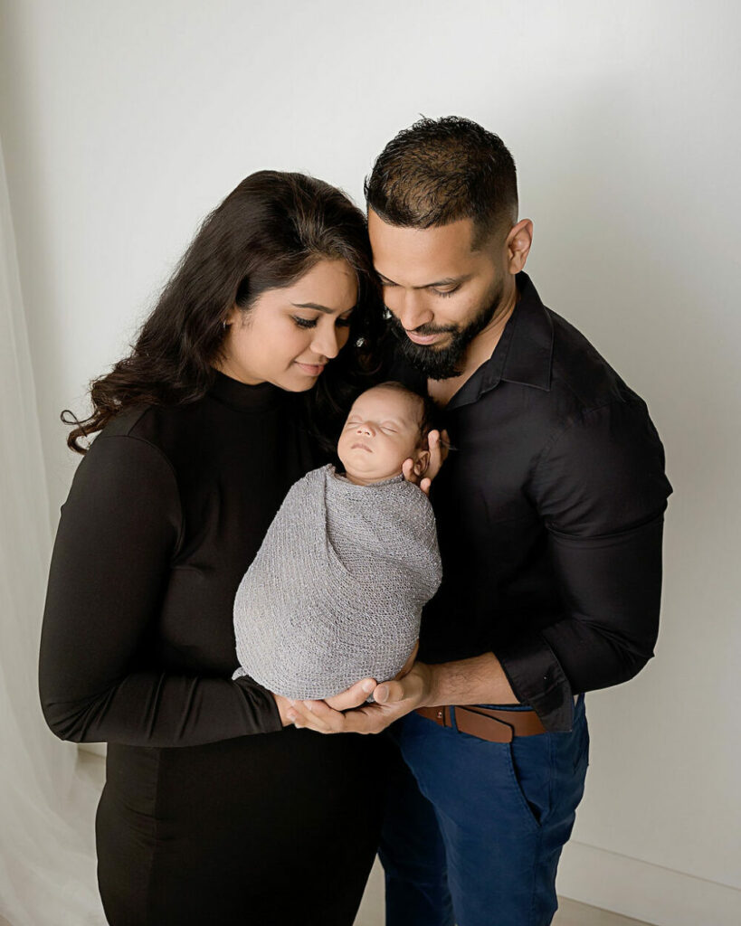 A man and woman looking down as they both hold their new baby, posing for their newborn baby photos for their newborn session in Deptford, New Jersey
