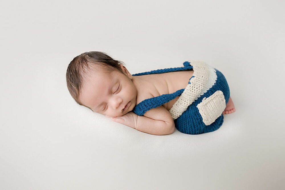Infant portrait of a boy sleeping on his belly with his hands tucked under his head wearing cute outfit and posed for his infant newborn session in wrightstown, New Jersey.