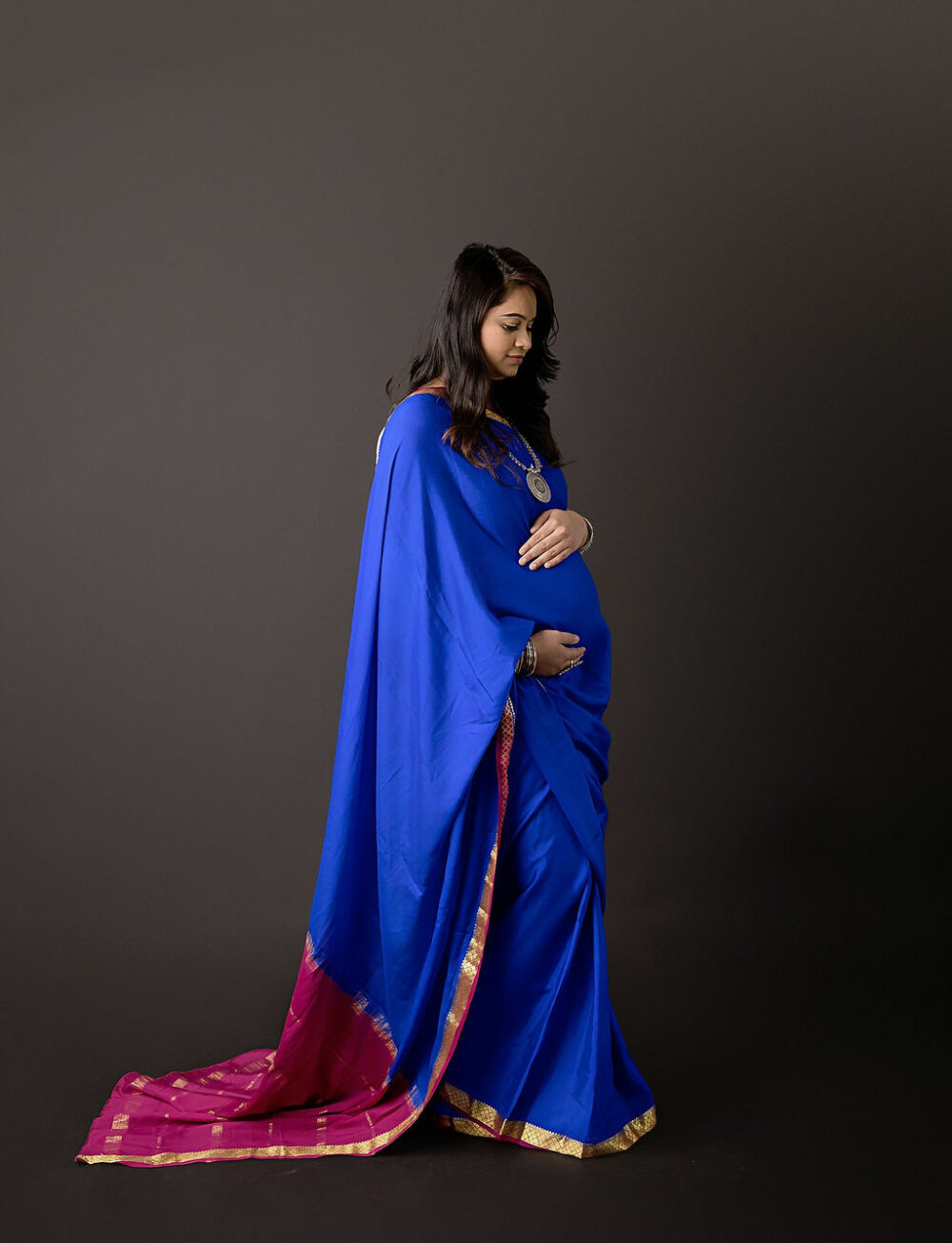 A woman standing and holding her belly, posing for her pregnancy portraits, wearing a sorry for her Indian inspired maternity session in Eastampton, new jersey.