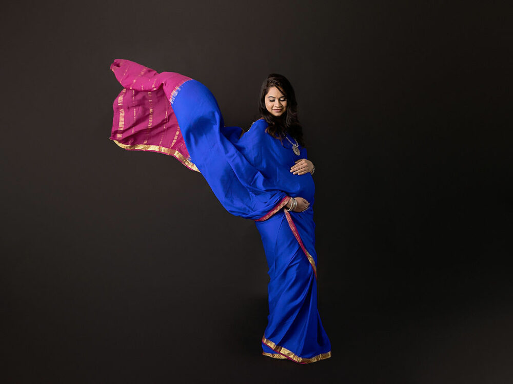 Maternity portrait of a woman standing at a 45-degree angle holding her belly and posing for her Indian maternity session in Freehold, New Jersey.