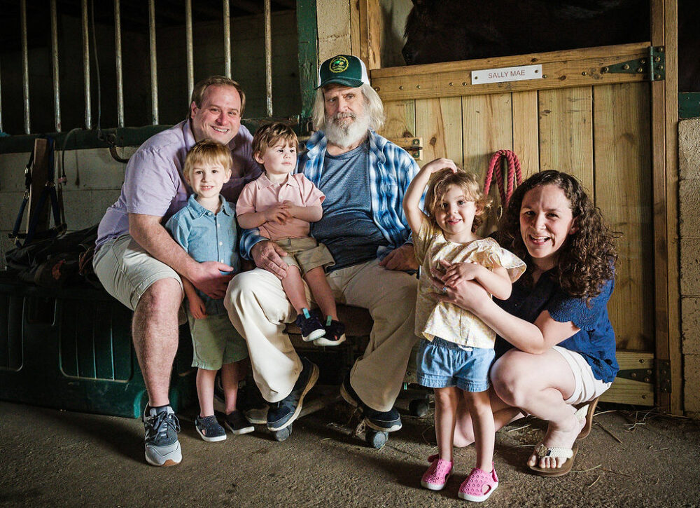 A couple and their three children sitting in a barn with their grandfather smiling for a Farm Lifestyle Family Session in Medford, New Jersey.