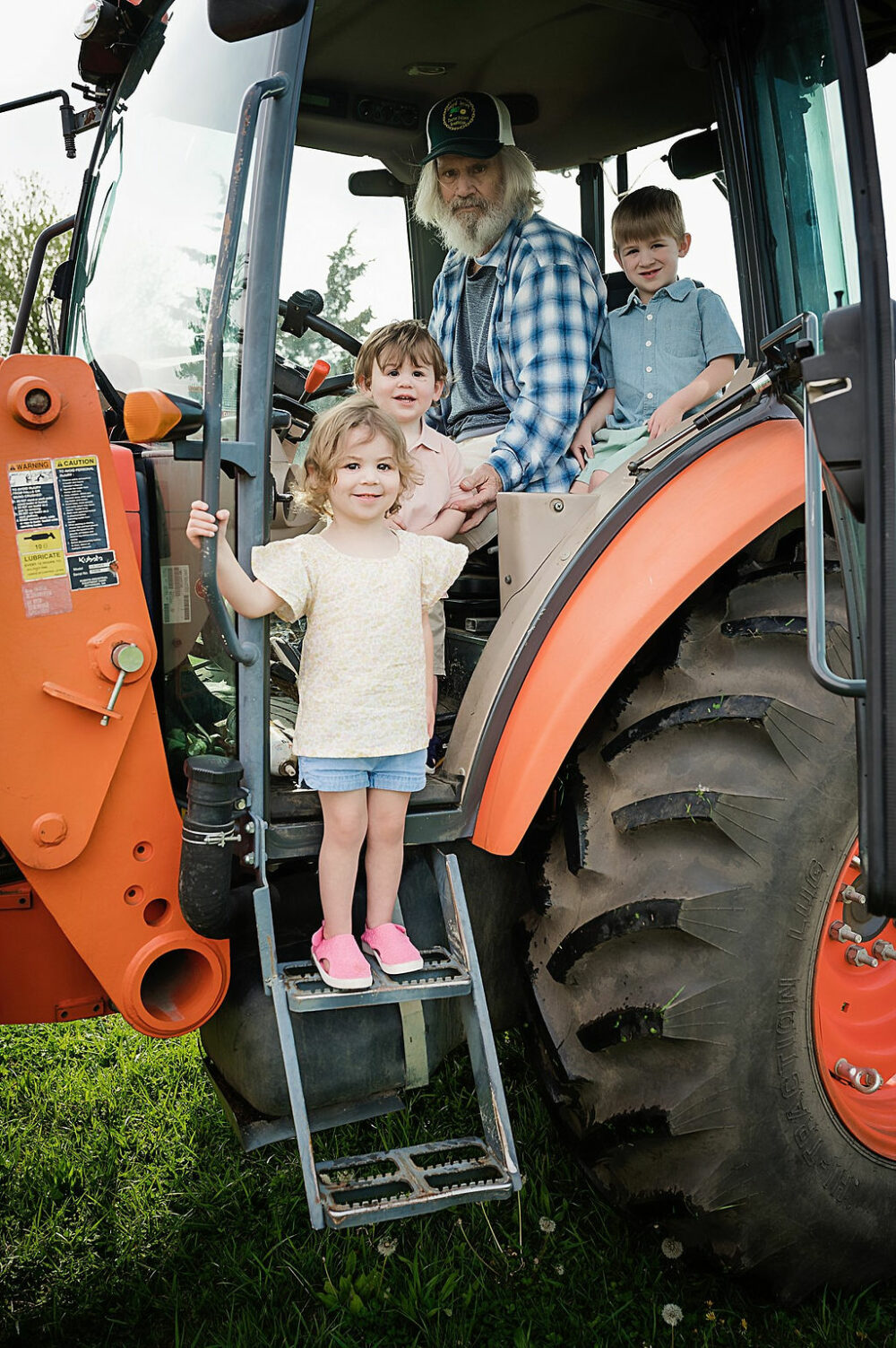 A man posing with his three grandkids in their tractor for a farm lifestyle family session in Cherry Hill, New Jersey.