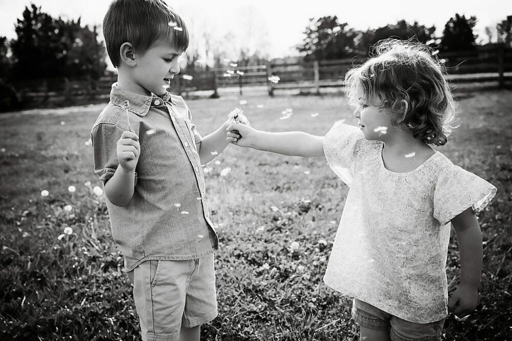 Black-and-white sibling portrait of a boy and girl holding hands and picking flowers during a farm lifestyle family session in Southampton, New Jersey.