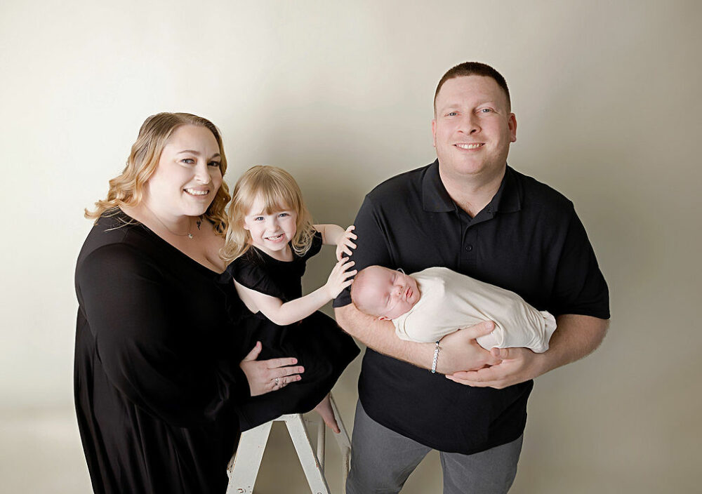 Family portrait of a man and a woman posing and smiling with their two children wearing matching clothing for a newborn photo shoot in Westampton, New Jersey.