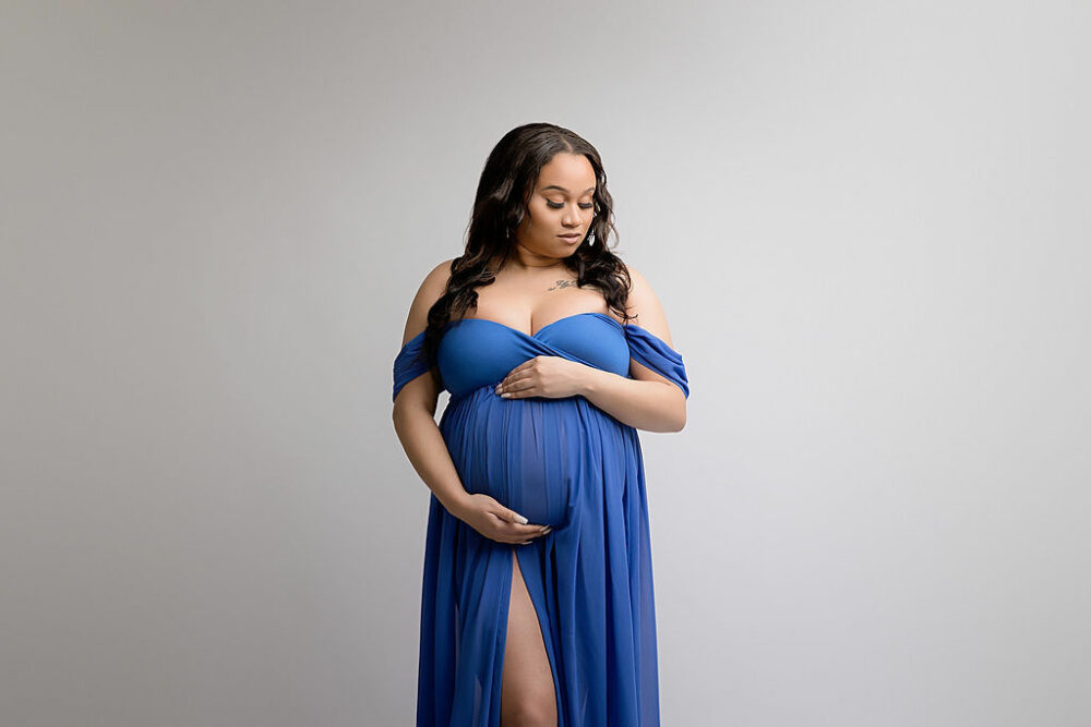 Woman standing and posing, wearing long gown and holding her belly for her maternity portraits in Camden, New Jersey.