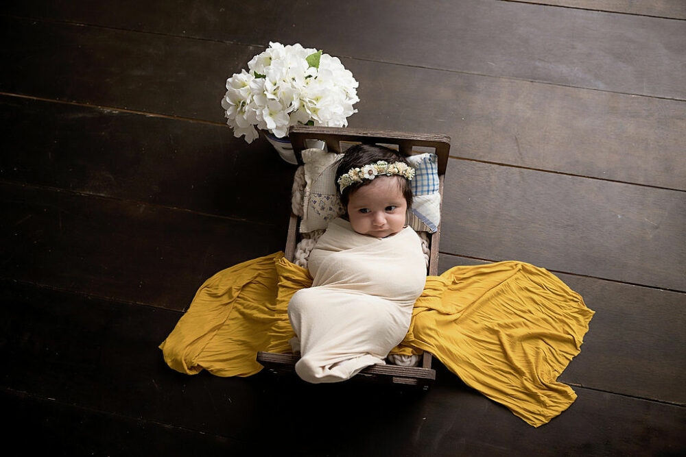 A infant placed in a small bed photography prop with flowers on the side, awake for her in-studio floral newborn session in Eastampton, New Jersey.