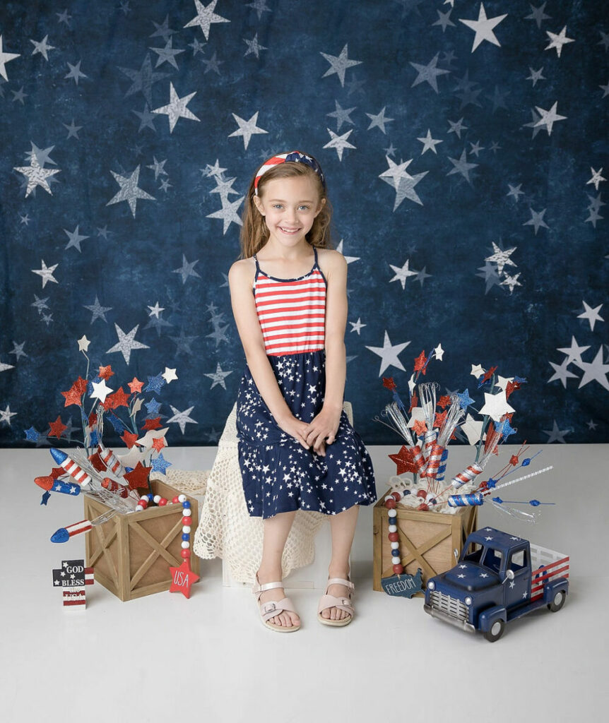 A girl sitting and smiling on photography prop as she sit in Fourth of July, set for her USA holiday mini sessions in Southampton, New Jersey.