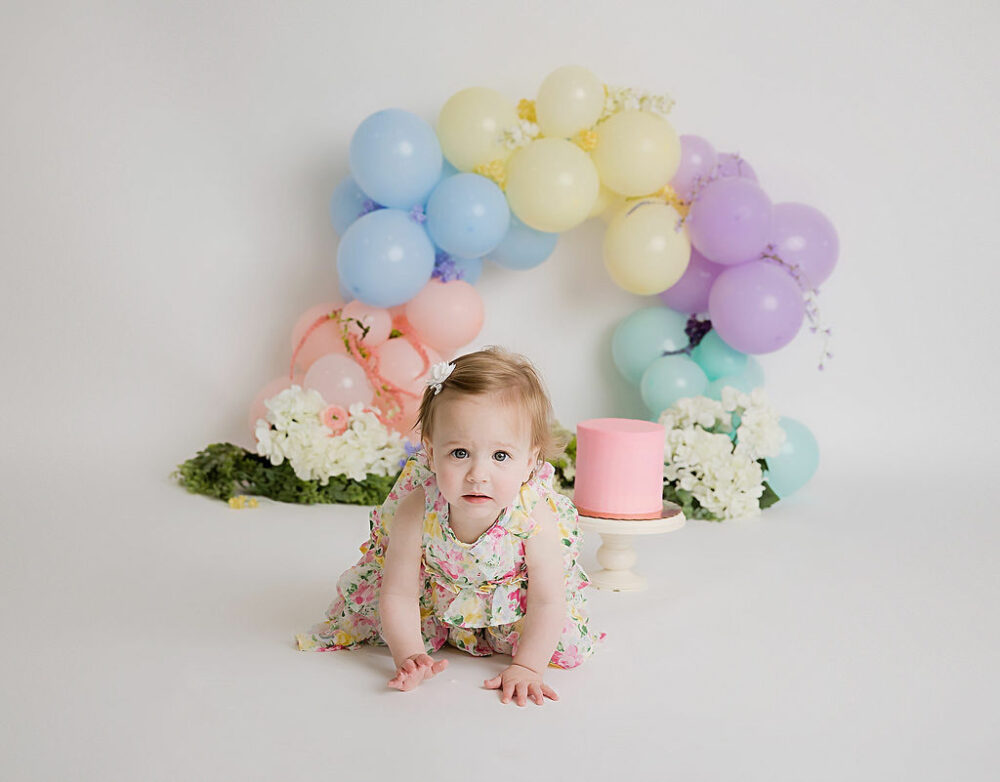 A cake smash picture of a girl eating her first cake with a garland as a backdrop with greenery for her first birthday party ideas in Pemberton, New Jersey.