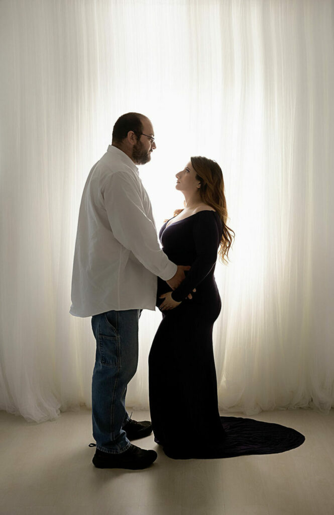 A man and woman facing each other and posed for a classy in-studio maternity session in Southampton, New Jersey.