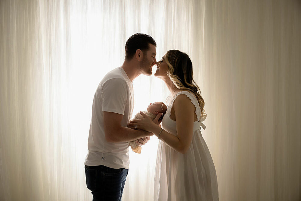 A family portrait of a woman and man touching noses and holding their new baby for baby photography session in Westampton, New Jersey.