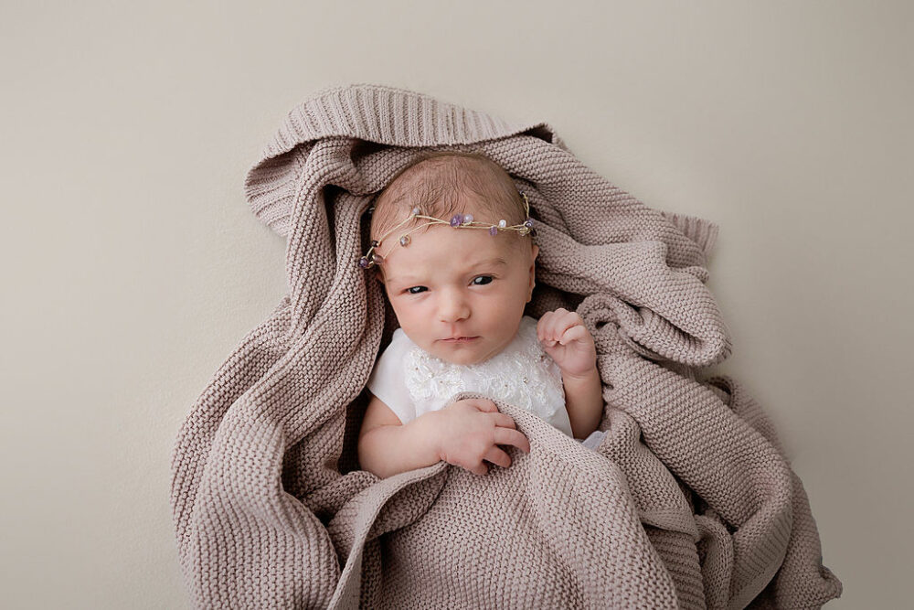 A cute picture of a newborn girl resting on blanket and wearing dainty headband for her in-studio rosy newborn session in Camden, New Jersey.