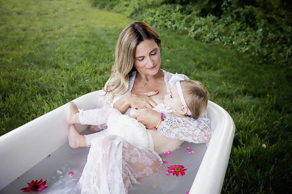 A woman looking lovingly at her daughter as she feeds her for it her lifestyle milk bath session outdoors in Eastampton, New Jersey.