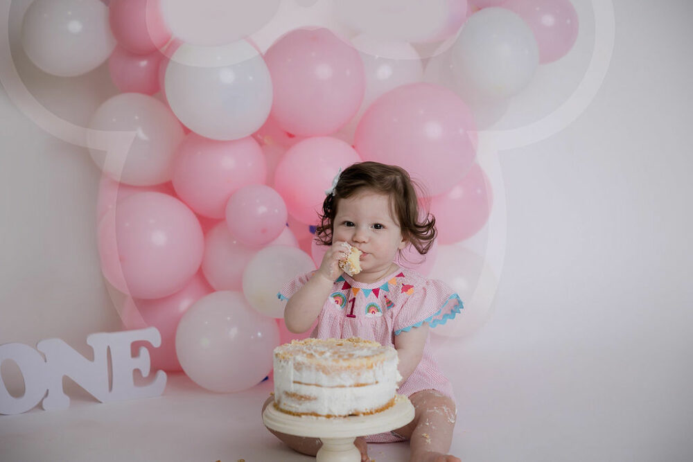 Cute picture of a girl, eating cake for her baby milestones photo shoot with a mini mouse theme in Westampton, New Jersey.