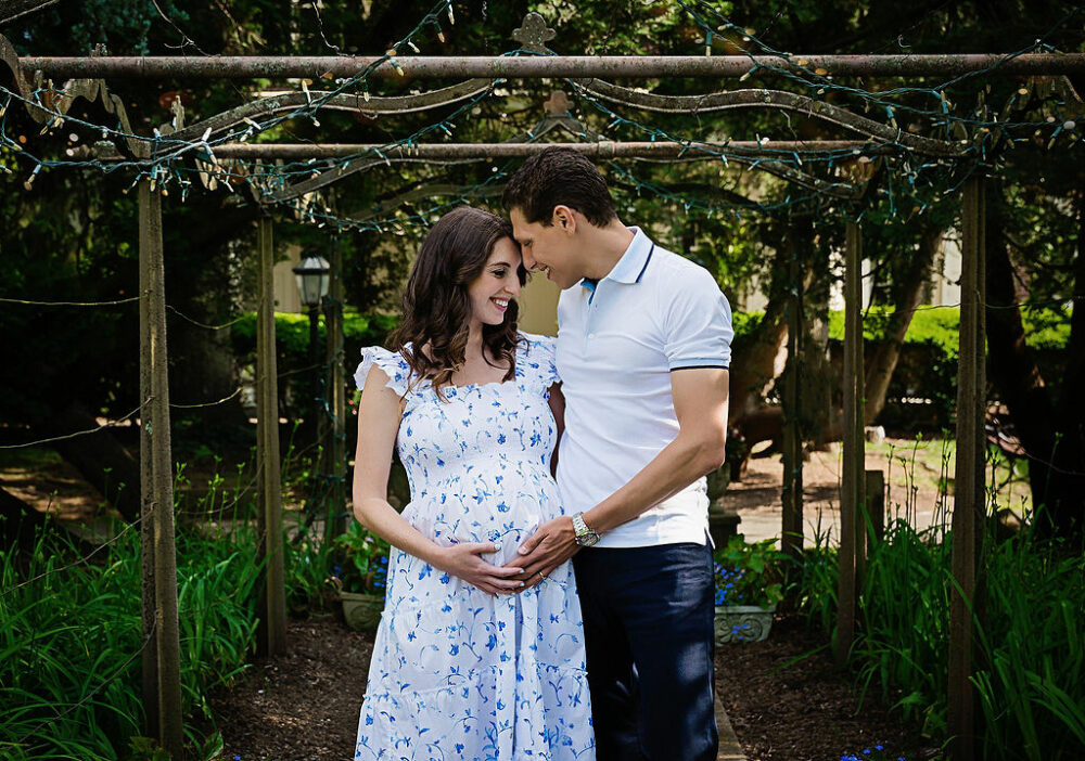 A man and woman posing in park trail touching foreheads and holding her belly for a outdoor maternity session in Smithville mansion in Mount Holly, New Jersey.