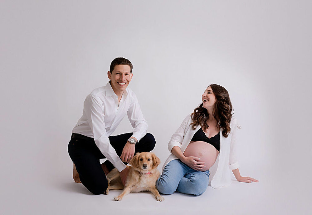 A lifestyle portrait of a couple sitting on the ground with their family dog for their maternity photo shoot ideas and Westampton, New Jersey.