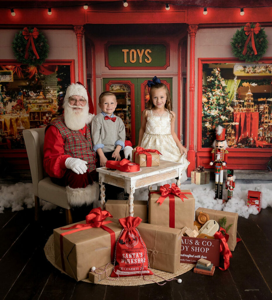 A sibling portrait of two toddler sitting with Santa Claus in Santa's workshop for a South Jersey Christmas Santa mini session in Eastampton, New Jersey.