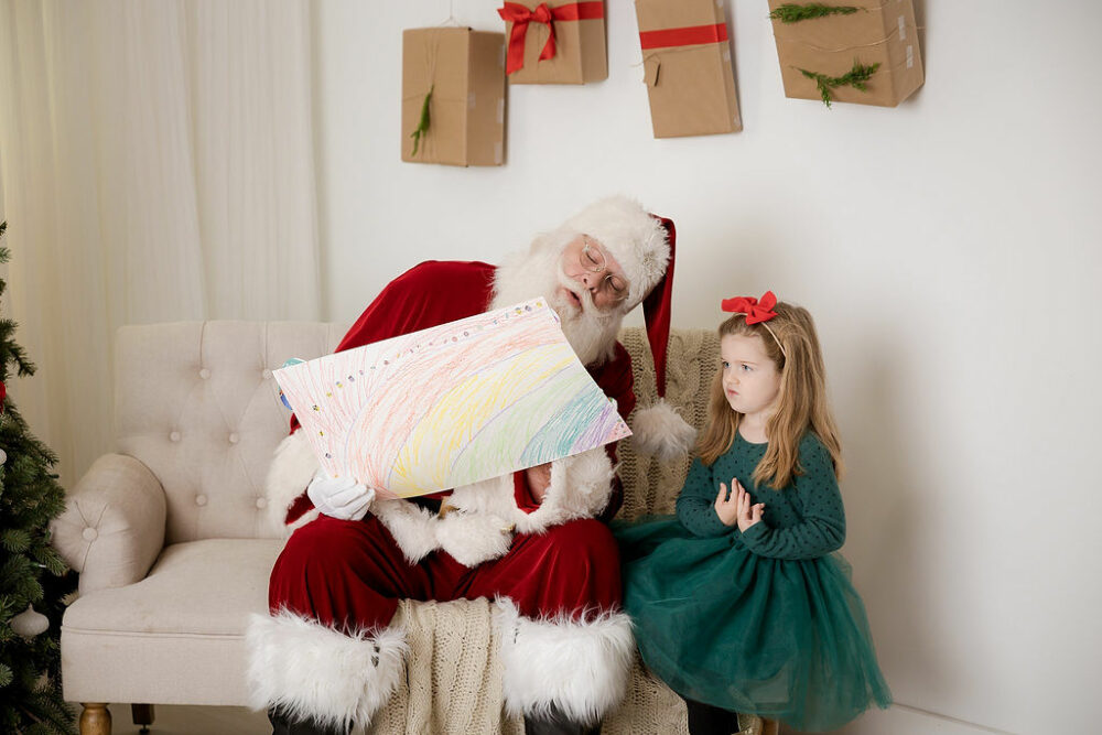 A picture of a girl showing Santa Claus a drawing that she did during her South Jersey Christmas Santa mini session in Deptford, New Jersey.
