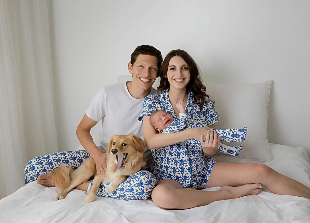 A couple posing with their new board and a dog wearing blue light pajamas in a bedtime photography set for their Blue newborn session in Eastampton, New Jersey.