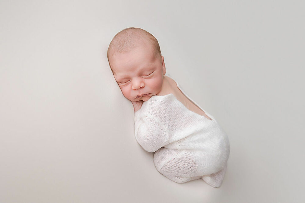 A newborn portrait of a boy wearing overalls sleeping on his tummy for his professional baby pictures taken during his newborn session in Hamilton, New Jersey.