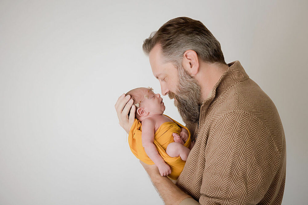 A man holding his newborn and looking at her face as she sleeps in his arms for a newborn session in Westampton, New Jersey.