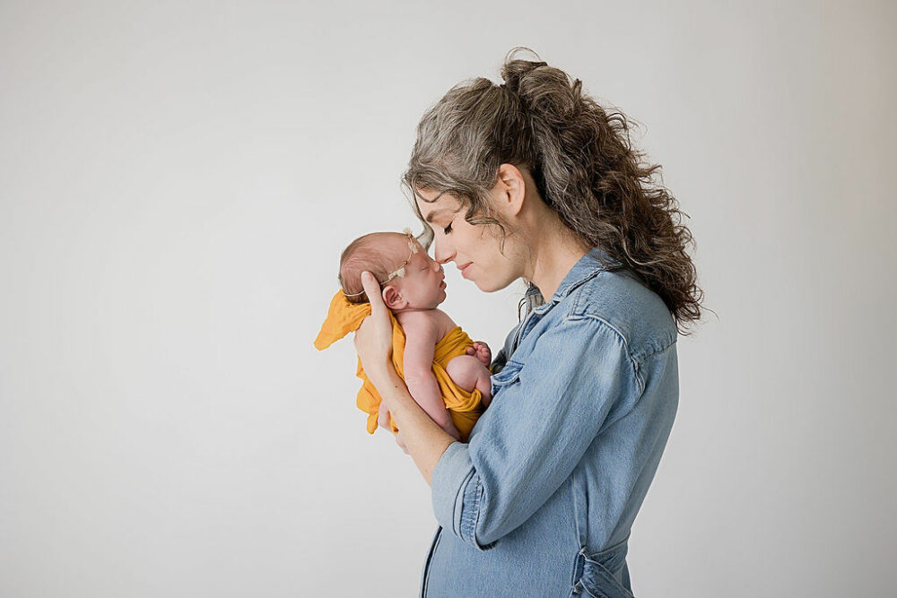 A woman standing to the side and touching noses with her infant who is wearing a headband and is wrapped for her sunflower newborn session in Eastampton, New Jersey.