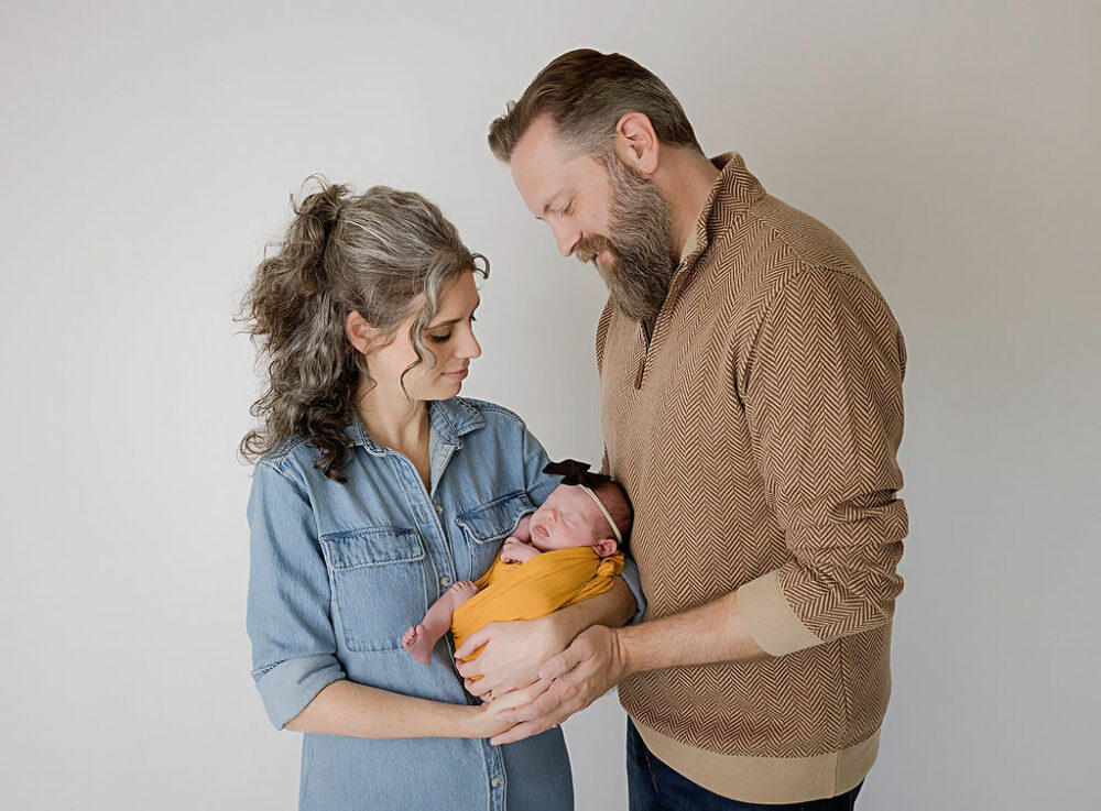 A family portrait of a man and woman looking at their newborn and she rest in between them for a fall family newborn photography in Medford, New Jersey.