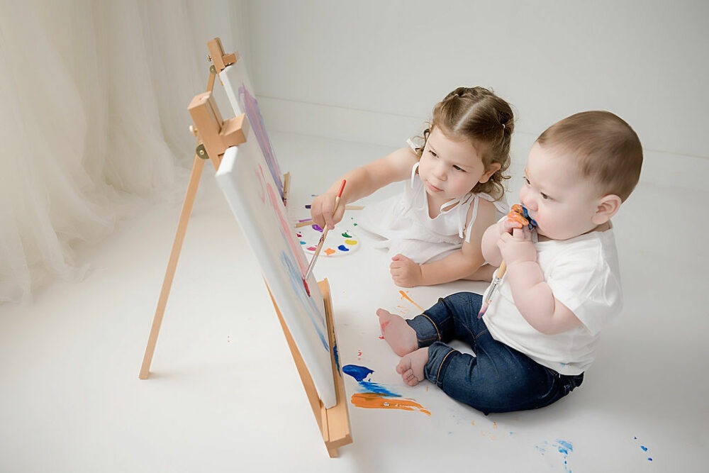 Cute picture of a boy and a girl painting during her milestone photo shoot for her third birthday images in professional studio in Westampton, New Jersey.