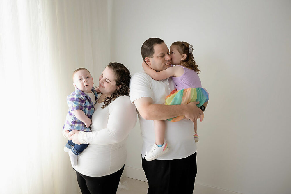A family portrait of a dad holding his toddler daughter and a mom holding their infant son posing for her colorful milestone session in Mount Holly, New Jersey.