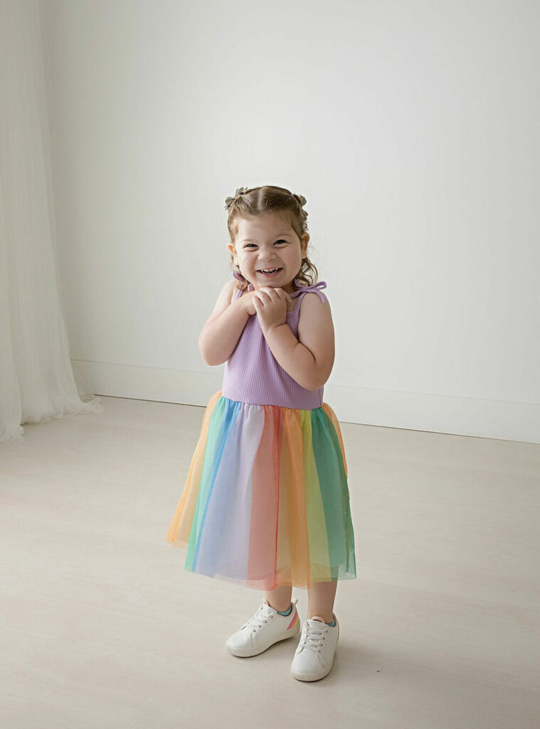 A cute picture of a girl smiling during her colorful milestone photography session wearing dress and tennis shoes for her portraits in Hamilton, New Jersey.