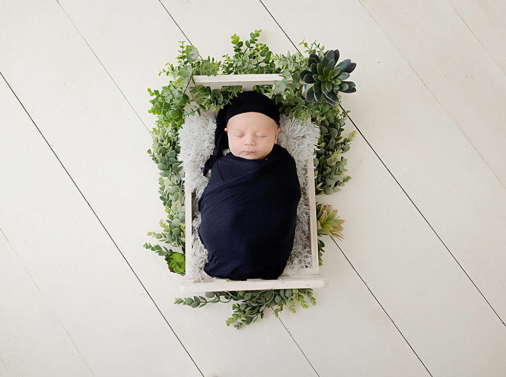 A infant sleeping and resting on textured blanket on top of tiny crib posed for his professional baby pics taken in Marlton, New Jersey.