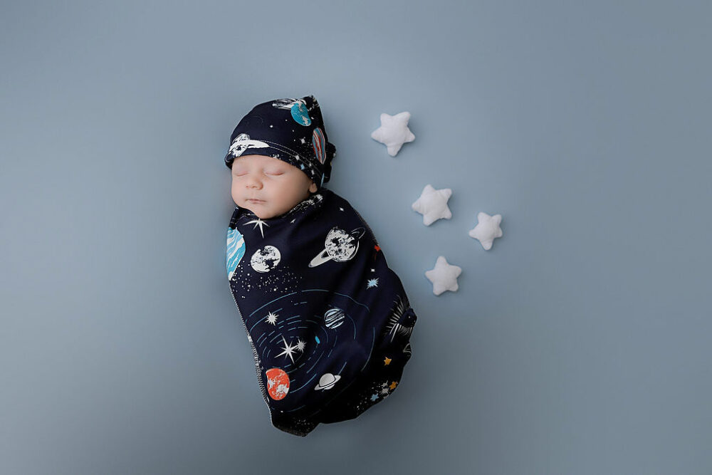 A newborn portrait of a boy in galaxy outfit and hat sleeping with stars around him or his newborn and family session eastampton, New Jersey.