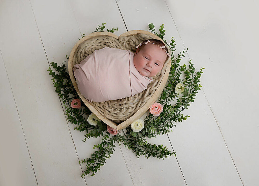 A sleepy girl resting on textured blanket inside heart shaped photography prop posed for her infant photography session with a princess theme in Tabernacle, New Jersey.
