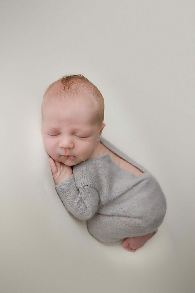 A baby boy resting on his tummy with knees tucked in wearing cute outfit for newborn photography session in Medford, New Jersey.