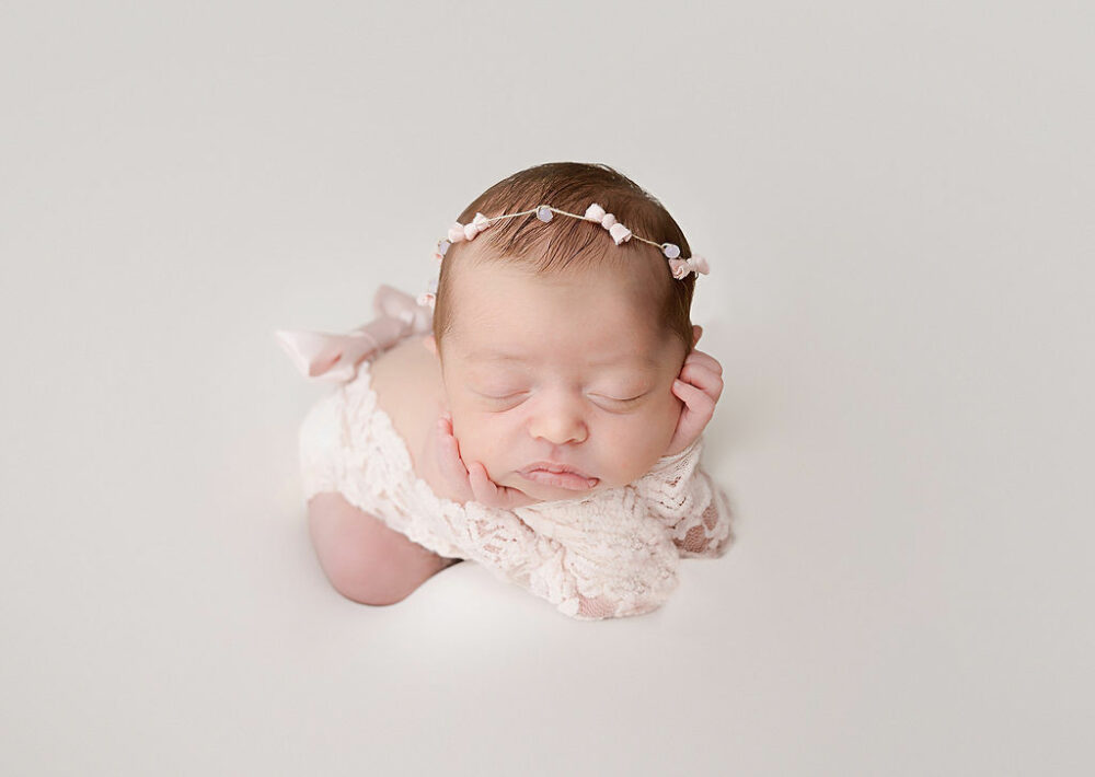 Cute newborn portrait of a girl propped up on her elbows and resting on her tummy as she sleeps during her pink newborn session in Hamilton, New Jersey.