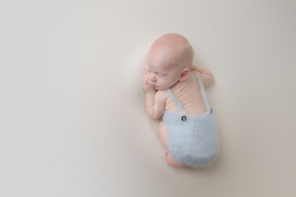 A close-up picture of a baby boy sleeping on his tummy wearing a cute outfit for his two minutes light blue newborn session in Wrightstown, New Jersey.