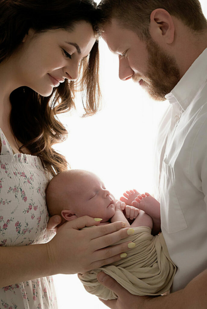 A close-up picture of a couple touching foreheads and holding their newborn in between them for their professional photographer/newborn pictures taken in Cherry Hill, New Jersey.