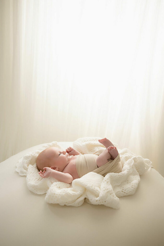 A baby boy, awake and resting on beanbag photography, prop, resting on textured blanket, and partially wrapped for his professional studios near me in South Jersey.