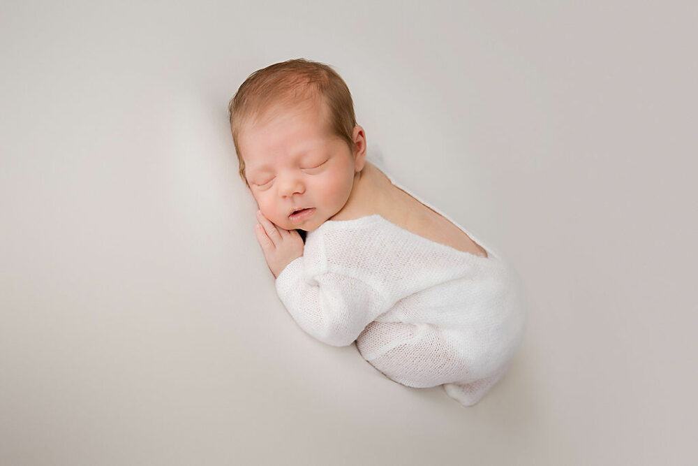 A newborn boy sleeping on his tummy with his knees tucked in wearing baby outfit for his professional newborn photography session in Tabernacle, New Jersey.
