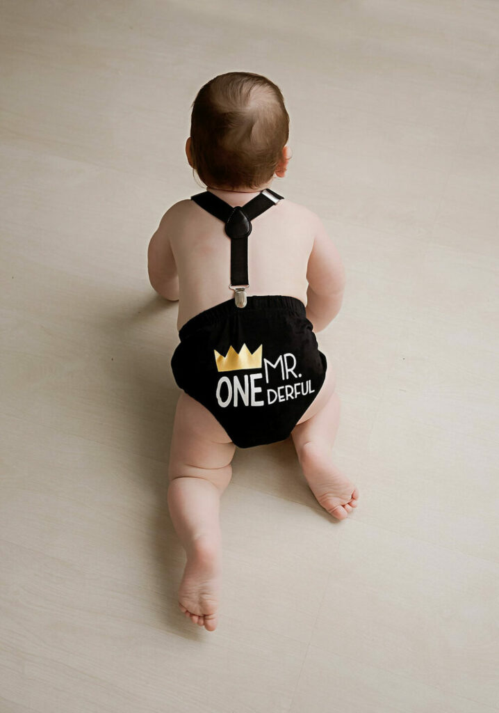 A boy crawling on the floor wearing an outfit that has Mr. Onederful printed on it for his milestone photoshoot in Southampton, New Jersey.
