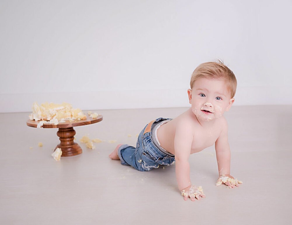 A cute picture of a one year old boy with a messy face, crawling by a cake for his cake smash photo shoot in Mount Holly, New Jersey.