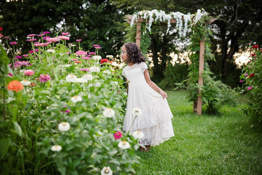 A cute photo of a girl wearing dress and smelling a flower in a flower garden for her mini session in Eastampton, New Jersey.