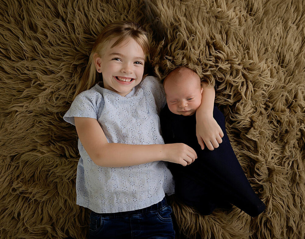 A sibling portrait of a big sister and her newborn brother together on a textured blanket posing for his newborn pics taken in Deptford, New Jersey.