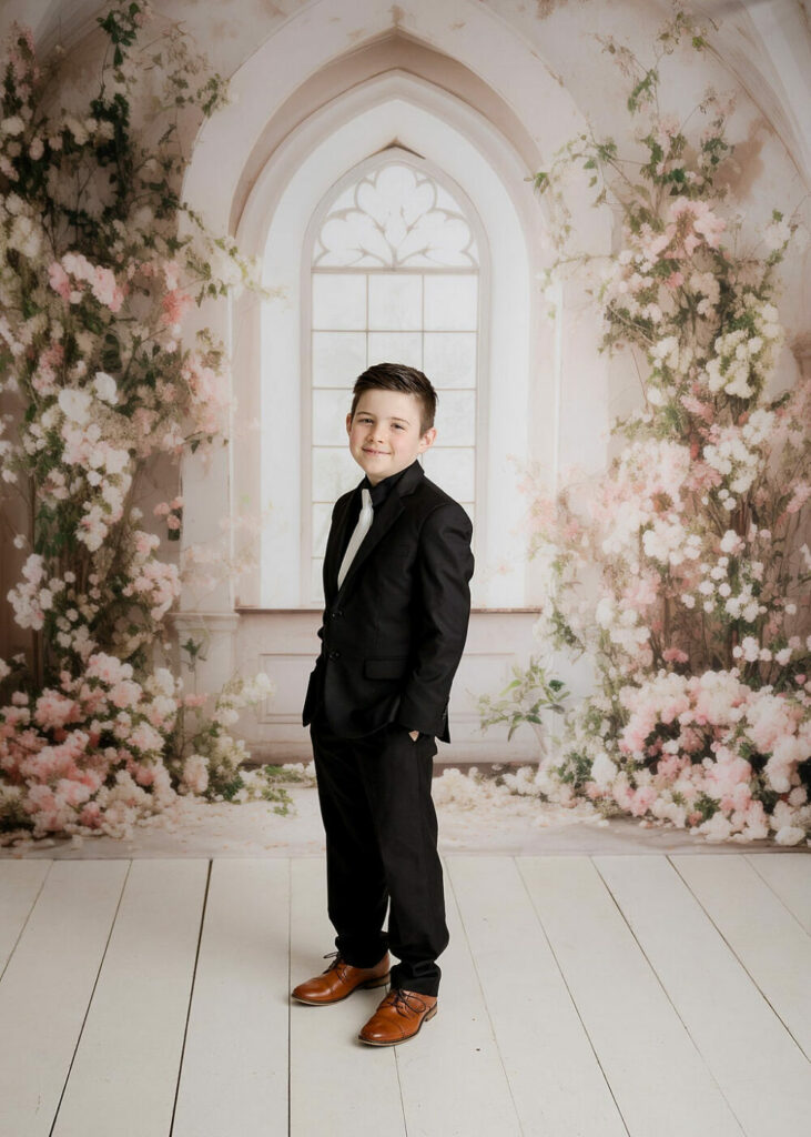 A boy standing and wearing a suit with his hands in his pockets and smiling for his Communion Mini Session in Southampton, New Jersey.