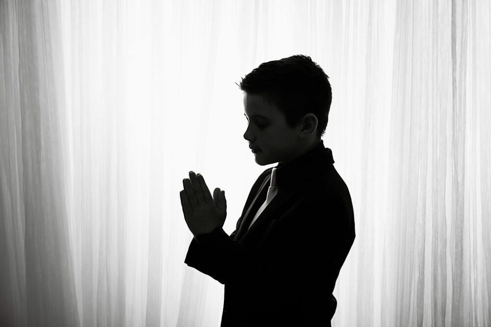 A close-up of a boy standing sideways, and looking down at prayer hands for his communion mini session in Hamilton, New Jersey.