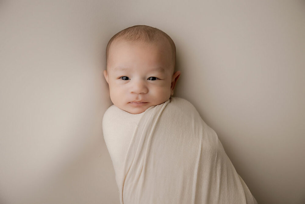a close-up of a boy swaddled and laying on her back on bean bag photography prop for his professional, classy newborn session in Medford, New Jersey.