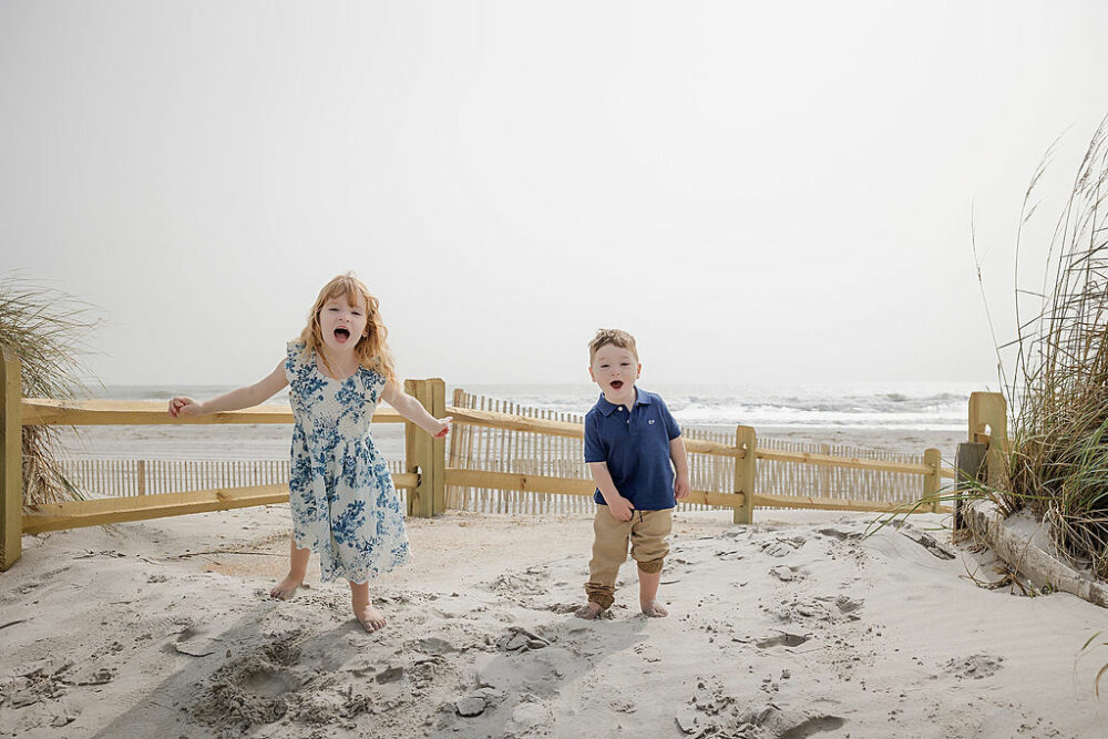 A sibling photo of a toddler girl and boy at the beach smiling for their lifestyle beach family session in Cape May, New Jersey.