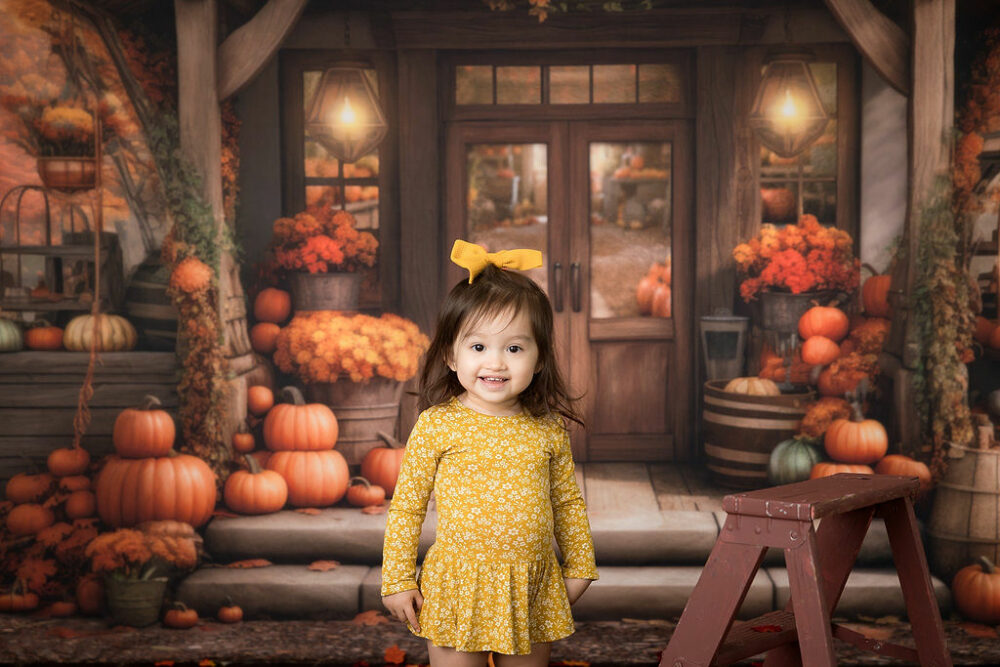 A smiling toddler girl wearing cute outfit and standing next to ladder prop for a fall in-studio mini session in Cherry Hill, New Jersey.