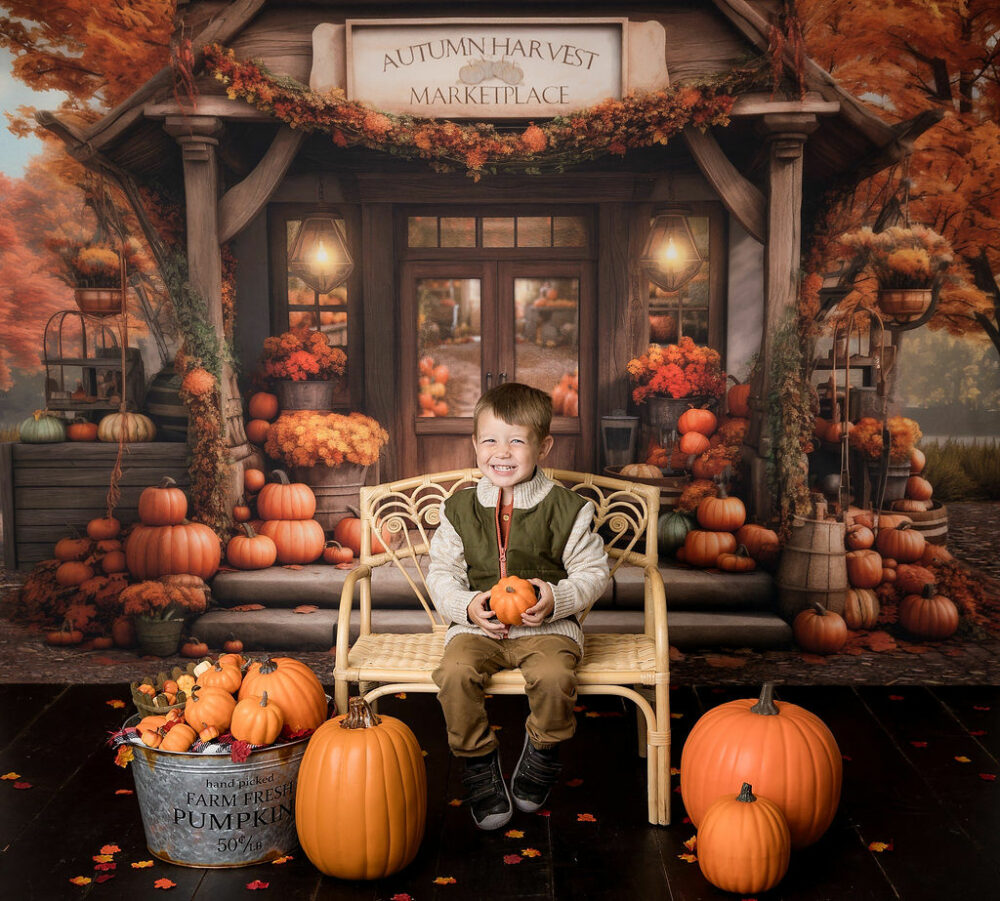A young boy sitting on tiny bench adorned with pumpkins props, with fall Autumn backdrop for seasonal in-studio fall mini session in Camden, New Jersey.